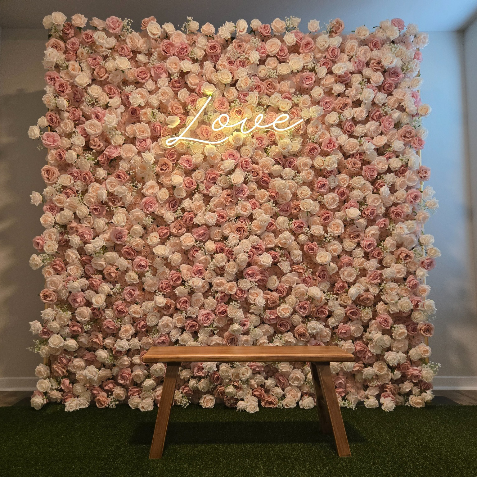 Blush flower wall with a glowing Love sign and wood bench